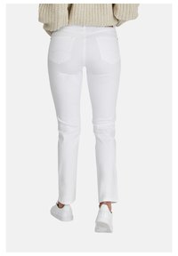 Jeans blancos ajustados con una textura suave, bolsillos traseros y detalles de costura sutiles. Combinar con zapatillas blancas completa el look.