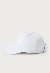 Hvit baseballcap med buet skjerm, laget av teksturert stoff. Har en subtil hevet logo foran og en justerbar stropp bak.