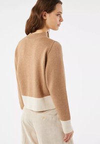 Maglione lavorato a maglia beige con orlo e polsini a costine color crema. Presenta un colletto rotondo e una vestibilità rilassata, abbinato a pantaloni di corduroy beige chiaro.