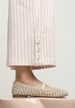 Ballerine in suede beige con embellishments di borchie argentate. Abbinate a pantaloni a righe rosa e bianche con dettagli di bottoni.