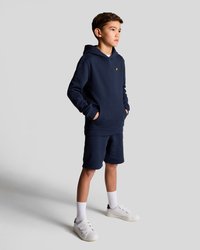 Navyblå hoodie och shorts-set i bomull, med en subtil gul logotyp på bröstet, matchat med vita sneakers och strumpor.