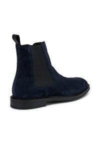 Botín Chelsea de ante azul marino con paneles elásticos en los laterales y una cinta de agarre; presenta una puntera redondeada y una suela baja de goma negra.