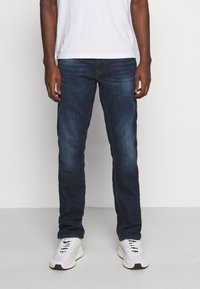 Mørkeblå denimjeans med rette ben, lett falming på lårene, fem lommer og kontrastsøm, kombinert med hvite joggesko.