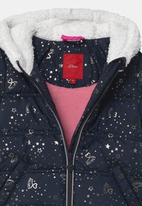 Veste rembourrée navy avec des motifs d'étoiles et de cœurs argentés, doublure intérieure de capuche en fourrure blanche et doublure intérieure rose. Fermeture éclair avec tirette en forme de cœur.