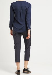 Mörkblå långärmad blus med en ryggfåll, ihopparad med slim fit mörka byxor och svarta lackskor med en texturerad sula.