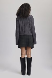 Szürke cable-knit crop pulóver hosszú ujjakkal, fekete kockás mini szoknyával és térdig érő fekete bőr csizmával párosítva.