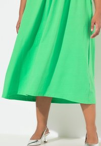 Vihreä puuvillamekko, jossa on hulmuava siluetti, lyhyet hihat ja helma, joka ulottuu juuri nilkkojen ylle. Yhdistetty hopeisiin korkokenkiin.