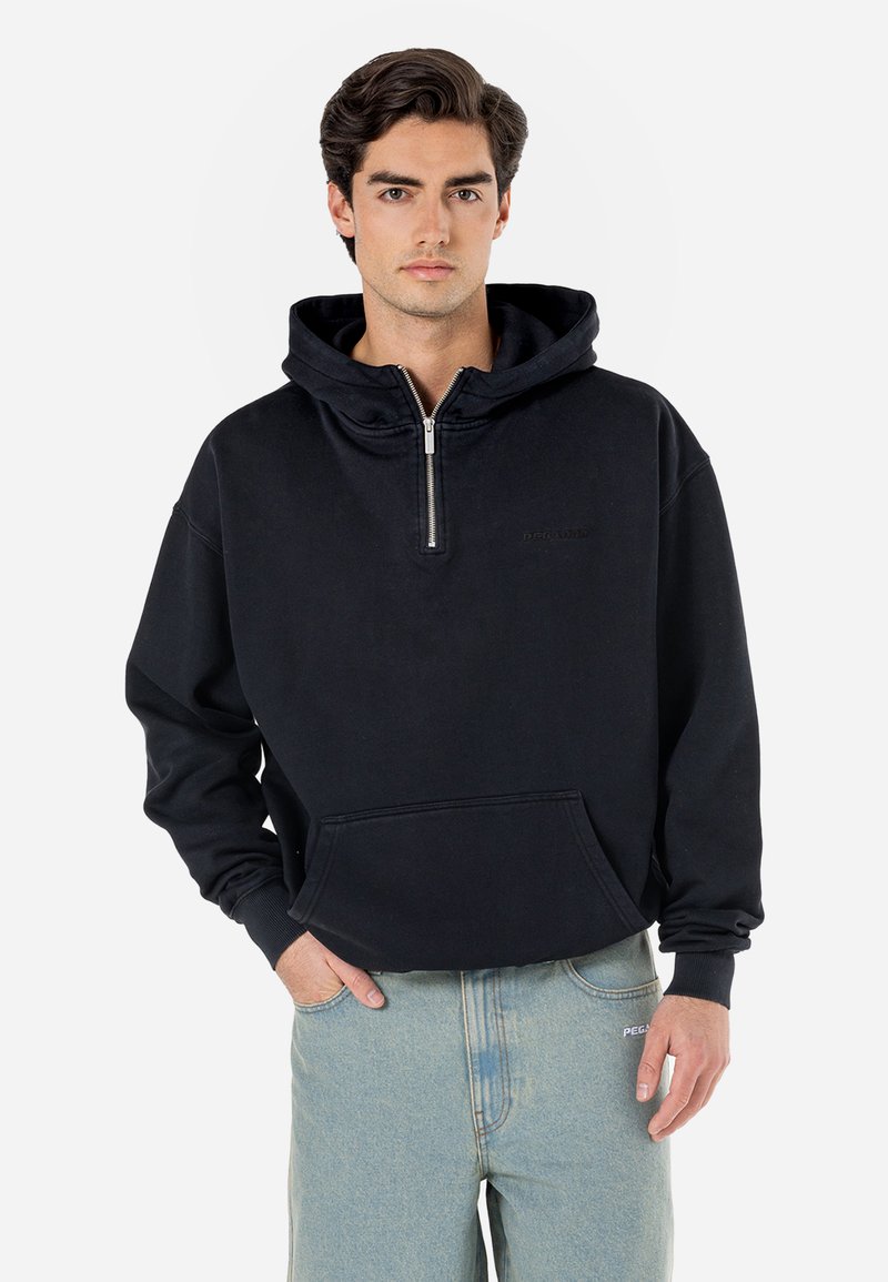 Sort zip-up hette med kengurulomme, snøring i hetten, og ribbede mansjetter, kombinert med lyseblå jeans. Myk stofftekstur.