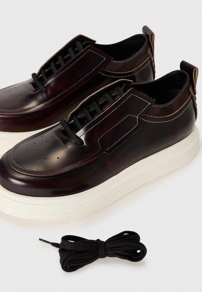 Chaussures en cuir bourgogne foncé avec une surface lisse, semelle plateformée blanche surélevée et lacets noirs. Présentent des accents de surpiqûres décoratives.