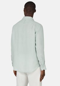 Camicia verde chiaro a maniche lunghe realizzata in un tessuto testurizzato, con un orlo curvo, polsini con bottoni e colletto classico.