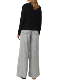 Czarny dzianinowy sweter z okrągłym dekoltem i prążkowanym obszyciem u dołu, zestawiony z luźnymi, jasno-szarymi dżinsami z tylnymi kieszeniami.