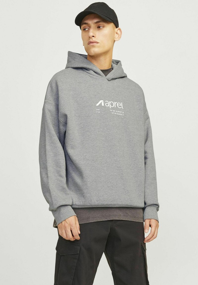 Sweat-shirt gris à capuche, avec un logo imprimé sur le devant. Poignets et ourlet cousus, associé à un pantalon cargo noir.