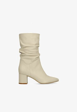 Crèmekleurige leren laars tot halverwege de kuit met een losvallend bovenwerk, een afgeronde neus en een blokhak met een lichtbruine zolenrand.
