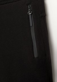 Tissu noir avec une finition texturée, doté d'une poche zippée de la même couleur noire. La fermeture éclair présente un design élégant.