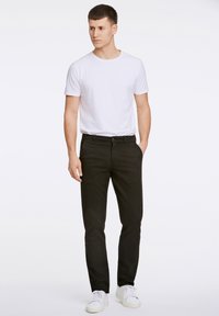 Črne kavbojke iz jeansa s prileganim krojem, ravnim rezom in petimi žepi. Kombinirane s preprosto belo majico z okrolim izrezom in belimi supergami.