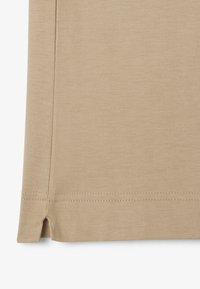 Beige t-shirt med ett mjukt, texturerat tyg. Har sidsprickor vid fållen och dubbelsydda sömmar för hållbarhet.