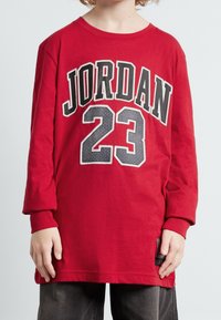 Punainen pitkähihaine T-paita, jossa on mustalla ja valkoisella letteringillä "JORDAN" ja "23", valmistettu pehmeästä kankaasta, rento istuvuus ja ribbikuvioidut hihansuut.