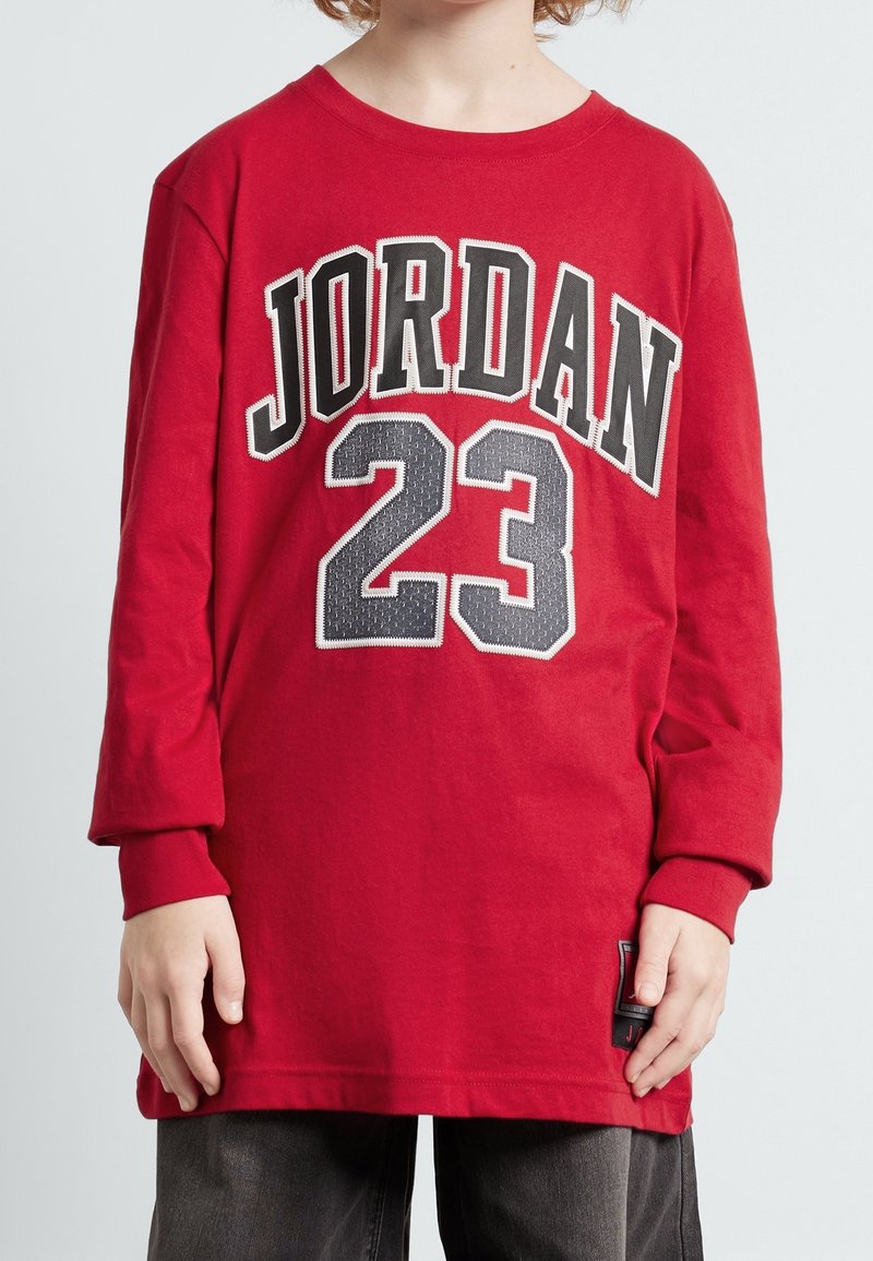 Punainen pitkähihaine T-paita, jossa on mustalla ja valkoisella letteringillä "JORDAN" ja "23", valmistettu pehmeästä kankaasta, rento istuvuus ja ribbikuvioidut hihansuut.