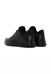 Zapatillas negras de cuero suave con una parte trasera de malla texturizada. Presentan una puntera redondeada, cierre de cordones y suelas acolchadas con ventilación.