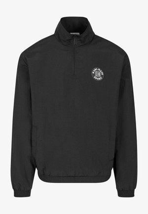 Melna viegla pusapļa jaka ar augstu apkakli un rāvējslēdzēju līdz krūtīm. Tai ir izšūts apļveida logs uz krūtīm un elastīgi aproces.