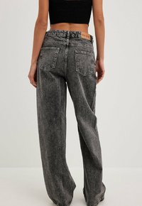 Jeans de pierna ancha en denim negro desgastado, con una cintura alta, diseño de cinco bolsillos y etiqueta de marca en la parte trasera. Textura y ajuste relajado.