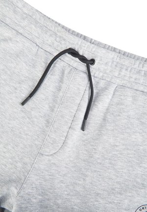 Hellgraue Jogginghose mit schwarzem, locker gebundenem Kordelzug und sichtbaren Seitentaschennähten.