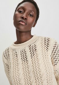 Cremfarbener gestrickter Pullover mit offener Maschenstruktur, Kabelmustern und geripptem Ausschnitt. Weiche Textur und entspannte Passform.