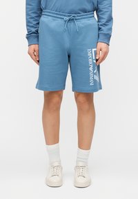 Ljusblå bomullsshorts med resårlinning och dragsko. Har en vit tryckt logotyp på vänster ben. Mjuk textur.