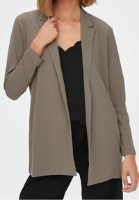 Khaki blazer, lange mouwen, open voorkant ontwerp, gladde stof, enkele knoopaccenten, gecombineerd met een zwarte top eronder.