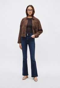 Chaqueta con estampado de leopardo marrón, top ajustado negro, vaqueros azul oscuro de talle alto y campana, y zapatos planos beige con punta; materiales suaves, diseño casual.