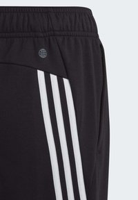 Pantaloni sportivi neri con strisce laterali bianche, vita elastica e tasche con zip. Tessuto morbido con una texture liscia. Logo del marchio presente.