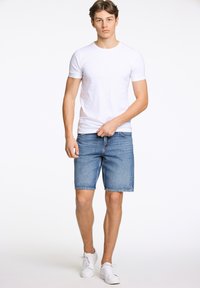Witte katoenen t-shirt gecombineerd met lichtblauwe denim shorts. De outfit wordt compleet gemaakt met witte sneakers. Eenvoudig, casual ontwerp en pasvorm.