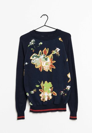 Pull bleu marine à manches longues avec grands imprimés floraux multicolores, poignets et ourlet côtelés avec une bande rouge, suspendu sur un cintre noir.