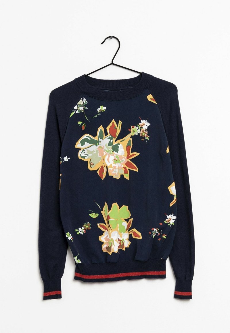 Pull bleu marine à manches longues avec grands imprimés floraux multicolores, poignets et ourlet côtelés avec une bande rouge, suspendu sur un cintre noir.