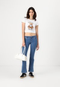 White cropped t-shirt with bear graphic, blue flared jeans, black sneakers with white accents, and a white handbag. Smooth materials.