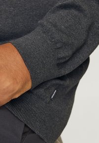 Dunkelgrauer, gestrickter Pullover mit gerippten Bündchen an Ärmeln und Saum. Verfügt über ein kleines Markenlabel auf Taillenhöhe. Weiche Textur und figurbetontes Design.