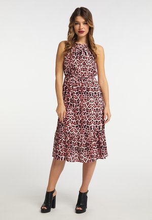 Kvinde iført ærmeløs midikjole i pink og sort leopardprint med samlet udskæring og sorte højhælede sko.
