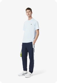 Lichtblauw katoenen T-shirt met een groen logo, gecombineerd met marineblauwe sportbroek met witte zijstrepen en witte sneakers met zwarte letters.