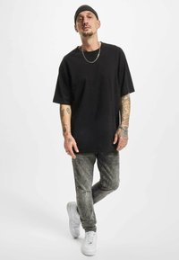 Un tricou oversize negru, blugi gri uzati și adidași albi. Prezintă tatuaje și un colier din argint, cu o căciulă pentru acoperirea capului.