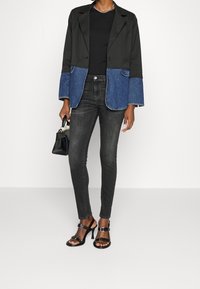 Blazer negro con mangas de mezclilla, combinado con jeans ajustados grises y sandalias de tacón negras. Incluye un pequeño bolso negro.