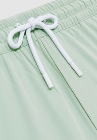 Hellgrüne Shorts mit elastischem Bund, weißem Kordelzug, der zu einer Schleife gebunden ist, und subtilen Nahtdetails.