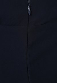 Hluboká modrá látka zblízka, s detaily zipu uprostřed nahoře, hladkým povrchem a jemným leskem, která ukazuje čistý, minimalistický design.