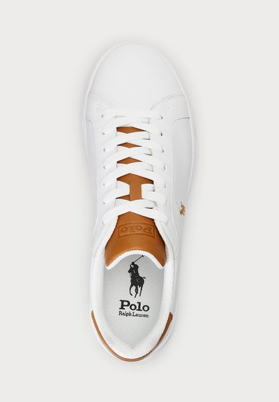 Hvit lær sneaker med brune detaljer, som har flate hvite snorer, en teksturert fôr, og en logo på innersålen og siden.