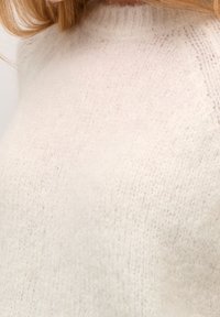 Maglione morbido di color crema con scollatura rotonda e tessuto texturizzato, caratterizzato da una finitura soffice e polsini a coste.
