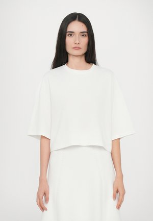 Tricou alb scurt din material moale, cu gât rotund și mâneci largi, asortat cu o fustă albă coordonată, cu detalii subtile.