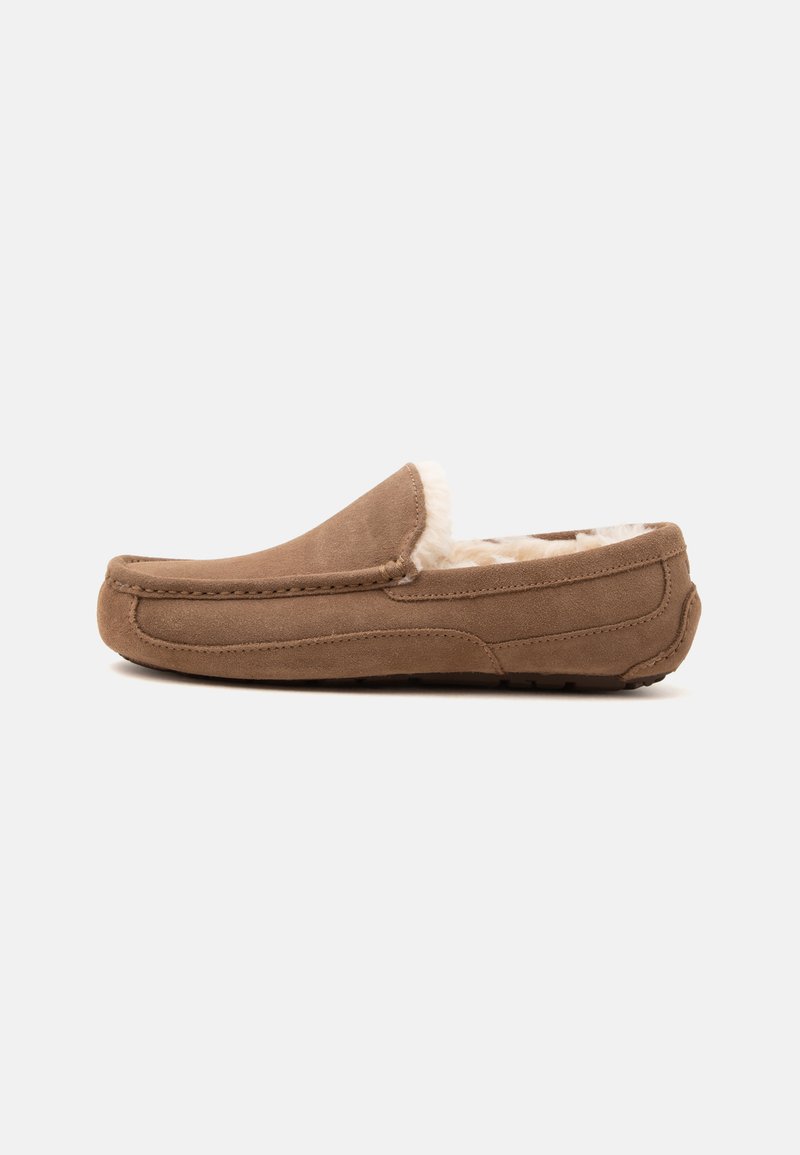 Chausson mocassin en daim marron avec doublure en polaire blanche et semelle en caoutchouc, présenté de côté sur un fond uni.