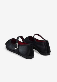 Zapatos suaves negros con punta redondeada, una correa con una hebilla plateada y una superficie texturizada. Presentan un interior rojo y costuras en la suela negras.