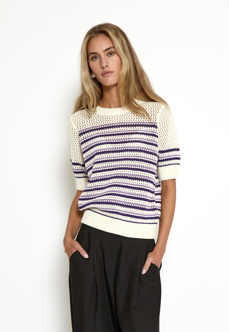 Suéter de manga corta de punto en crema con rayas horizontales moradas y azules marino. Presenta un patrón texturizado y un dobladillo acanalado. Se lleva con pantalones negros.