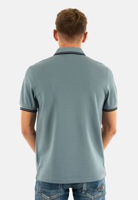Polo in azzurro chiaro con maniche corte, con collo e orlo a righe nere. La vista posteriore mostra una texture liscia e una vestibilità rilassata.