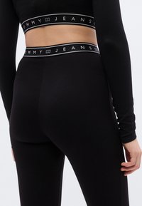 Μαύροι ριμπ κολάν με εφαρμοστή σχεδίαση και ελαστική μέση με το λογότυπο "TOMMY JEANS" σε λευκό κείμενο. Ομαλή υφή, χωρίς σχέδια.